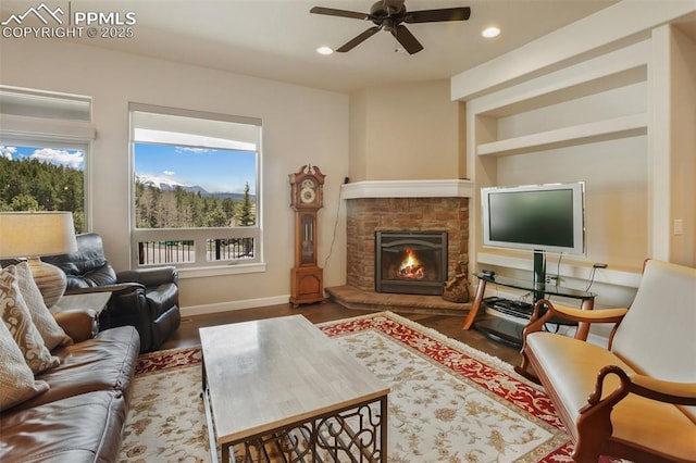 living room featuring baseboards, a ceiling fan, a stone fireplace, wood finished floors, and recessed lighting