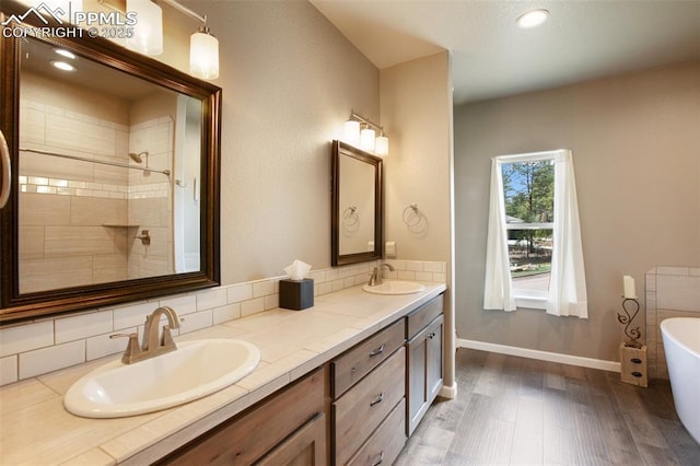 bathroom with wood finished floors, a soaking tub, double vanity, baseboards, and recessed lighting