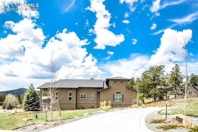 view of front of property featuring stucco siding, curved driveway, and a front yard