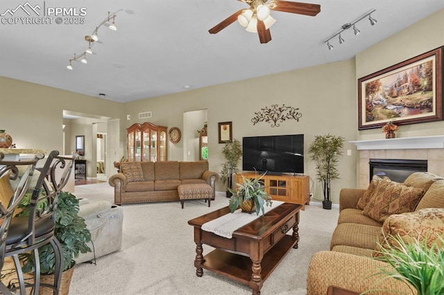 living room with track lighting, ceiling fan, carpet floors, and a tiled fireplace