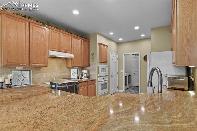 kitchen with under cabinet range hood, white appliances, washer / clothes dryer, light stone countertops, and recessed lighting