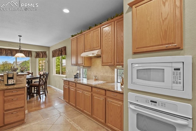 kitchen with white appliances, under cabinet range hood, recessed lighting, baseboards, and light stone countertops