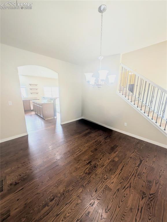 unfurnished dining area featuring a chandelier, dark wood-type flooring, baseboards, and arched walkways