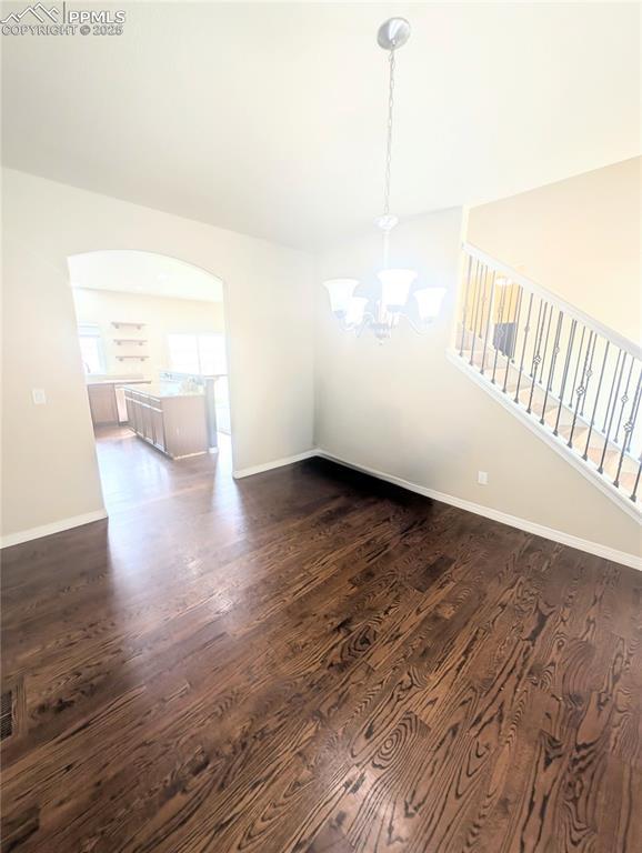unfurnished dining area featuring a chandelier, dark wood-type flooring, baseboards, stairs, and arched walkways