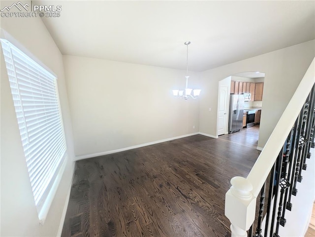 unfurnished dining area with dark wood-style floors, a chandelier, arched walkways, and baseboards