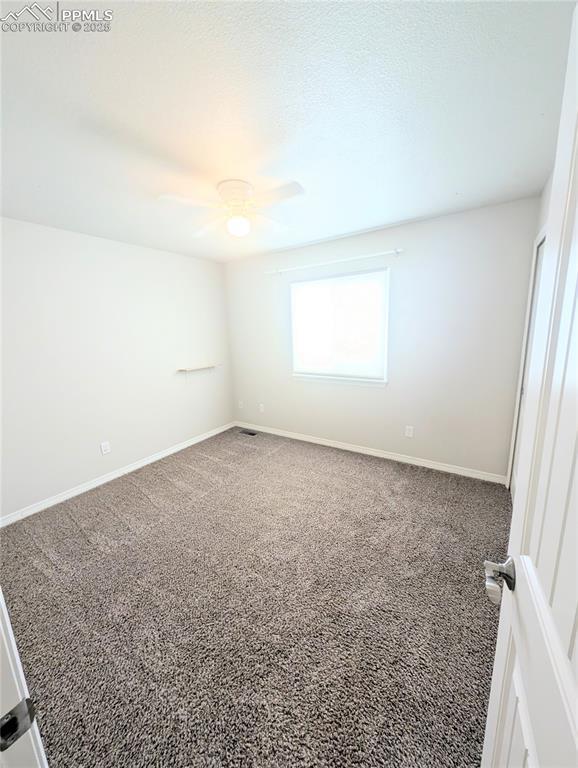 carpeted empty room featuring a ceiling fan and baseboards