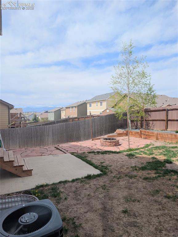 fenced backyard with a fire pit, a patio, a residential view, and central air condition unit