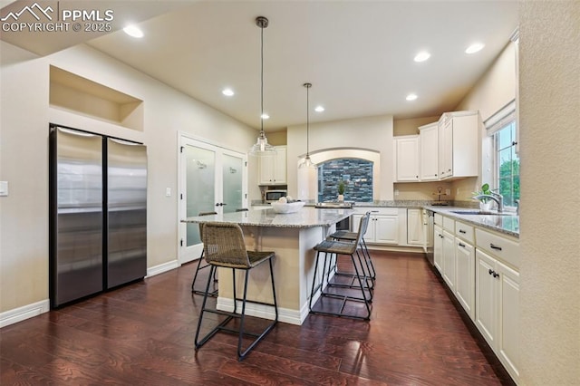 8451 Meadow Wing Cir, Colorado Springs, CO 80927 - kitchen with appliances with stainless steel finishes, white cabinetry, light stone countertops, a sink, and dark wood finished floors
