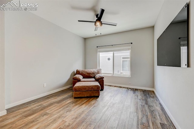 living area featuring wood finished floors, baseboards, and ceiling fan