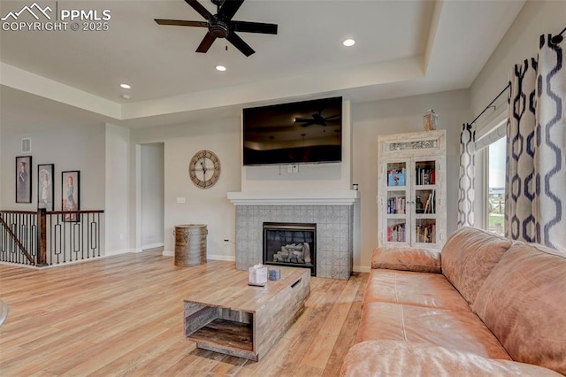 living room with ceiling fan, wood finished floors, a tiled fireplace, recessed lighting, and a raised ceiling