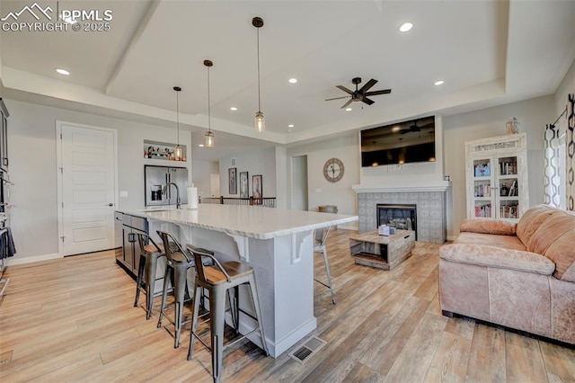 kitchen featuring a tray ceiling, light countertops, a ceiling fan, a kitchen bar, and recessed lighting