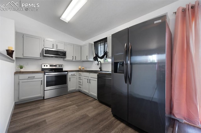 kitchen with stainless steel appliances, lofted ceiling, dark countertops, a sink, and dark wood-style flooring