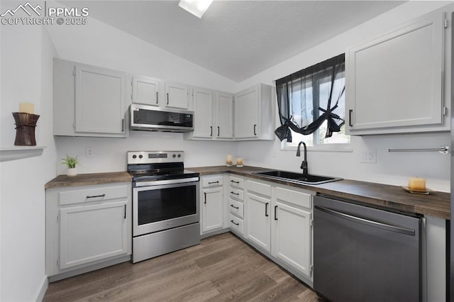 kitchen featuring stainless steel appliances, a sink, vaulted ceiling, butcher block counters, and wood finished floors