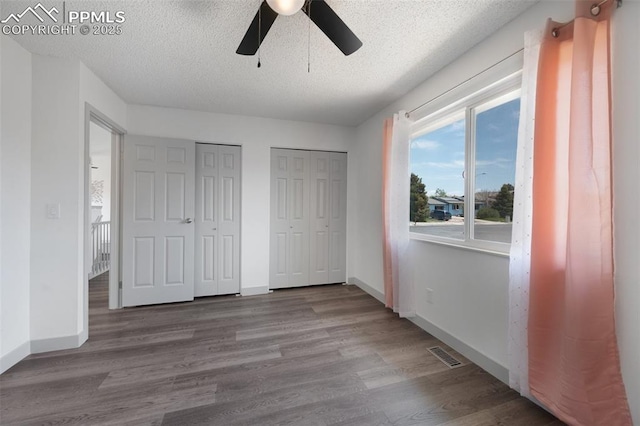 unfurnished bedroom featuring two closets, wood finished floors, a textured ceiling, baseboards, and a ceiling fan