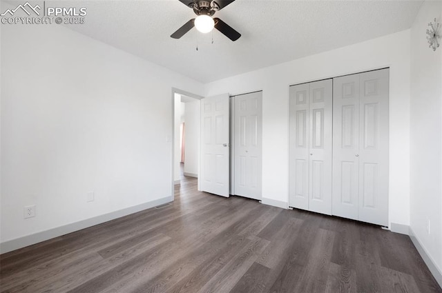 unfurnished bedroom featuring multiple closets, dark wood finished floors, baseboards, and a ceiling fan