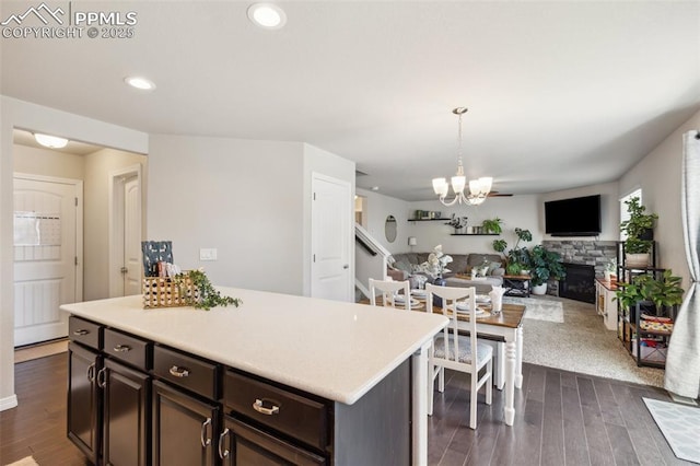 kitchen featuring light countertops, a stone fireplace, dark wood-style floors, a chandelier, and dark brown cabinets