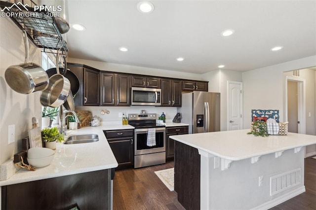 kitchen with stainless steel appliances, a sink, dark brown cabinetry, light countertops, and dark wood-style flooring