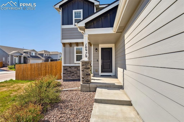 property entrance with board and batten siding, fence, a residential view, and stone siding