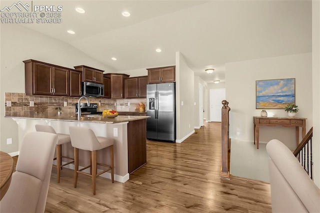 4473 Hessite Loop, Colorado Springs, CO 80938 - kitchen with appliances with stainless steel finishes, a peninsula, backsplash, wood finished floors, and lofted ceiling