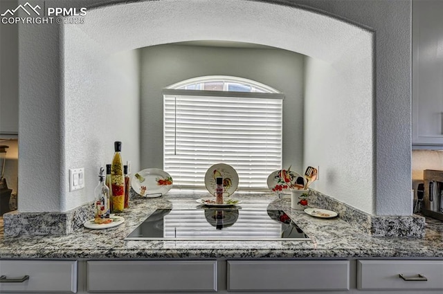 detailed view of black electric cooktop, light stone counters, and a textured wall