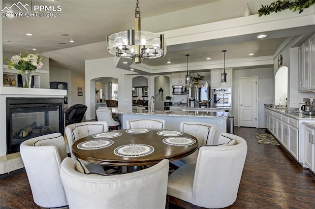 dining space with arched walkways, a chandelier, dark wood-style floors, recessed lighting, and a multi sided fireplace