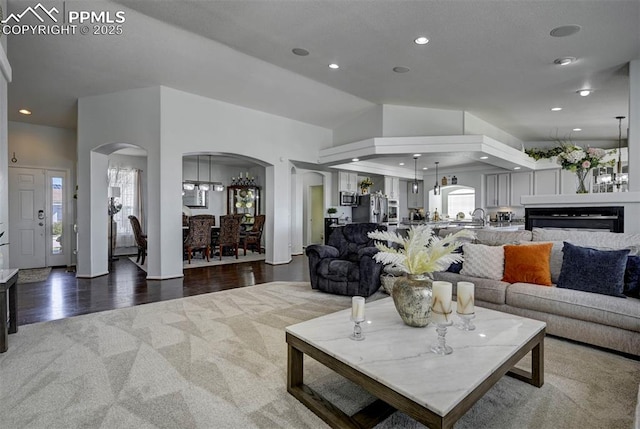 living area featuring arched walkways, wood finished floors, recessed lighting, high vaulted ceiling, and a fireplace