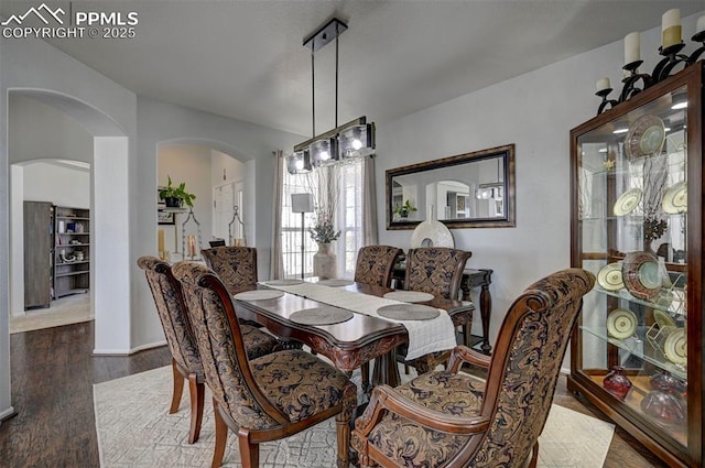 dining space with arched walkways and wood finished floors