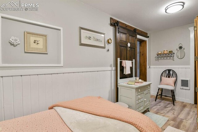 bedroom with a barn door, wainscoting, light wood-style flooring, and heating unit