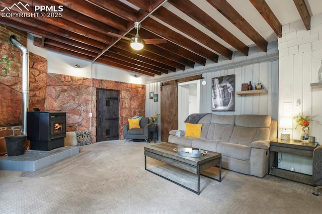 living area featuring carpet flooring, beamed ceiling, a wood stove, and ceiling fan