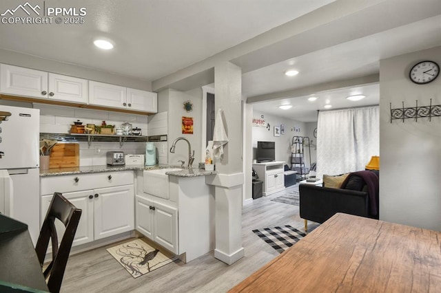 kitchen featuring light wood finished floors, a sink, white cabinets, decorative backsplash, and recessed lighting