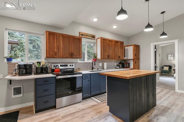 kitchen with stainless steel electric range oven, a sink, backsplash, light wood finished floors, and hanging light fixtures