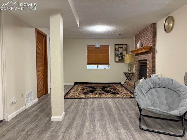 905 Hubbell Dr, Colorado Springs, CO 80911 - sitting room with wood finished floors, baseboards, a textured ceiling, and a brick fireplace