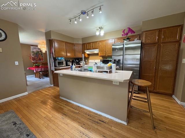 905 Hubbell Dr, Colorado Springs, CO 80911 - kitchen with appliances with stainless steel finishes, under cabinet range hood, light wood-type flooring, a chandelier, and brown cabinetry
