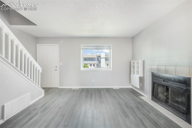 1223 Soaring Eagle Dr, Colorado Springs, CO 80915 - unfurnished living room with wood finished floors, a tiled fireplace, a textured ceiling, stairs, and baseboards