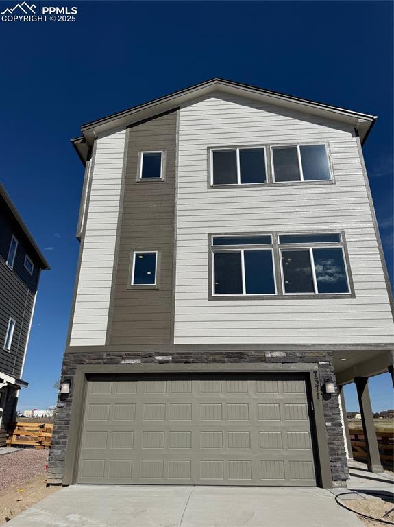 7371 Cornice Pt, Colorado Springs, CO 80923 - view of front of house featuring a garage, stone siding, and driveway