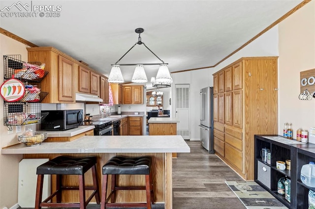 10635 Via Vaquaro Pt, Fountain, CO 80817 - kitchen with appliances with stainless steel finishes, under cabinet range hood, a peninsula, crown molding, and wood finished floors