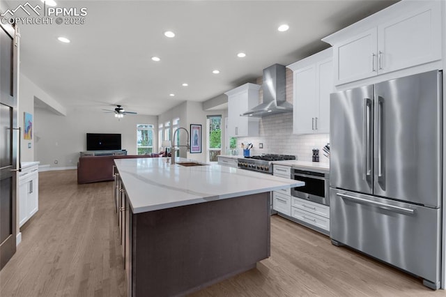 kitchen with stainless steel appliances, wall chimney exhaust hood, a sink, open floor plan, and a ceiling fan