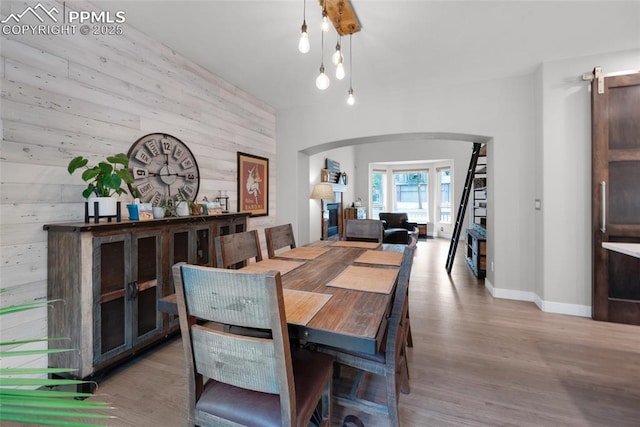 dining area with wooden walls, arched walkways, baseboards, and wood finished floors