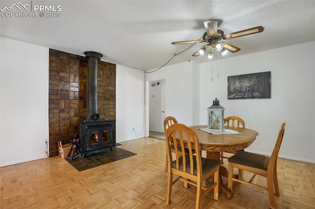 dining space featuring a wood stove, a ceiling fan, and a textured ceiling