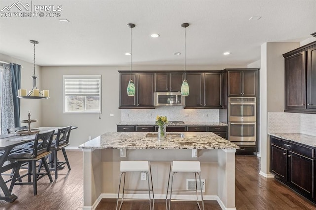 3197 Cool Meadow Pl, Castle Rock, CO 80104 - kitchen featuring appliances with stainless steel finishes, dark wood finished floors, dark brown cabinets, decorative backsplash, and light stone countertops