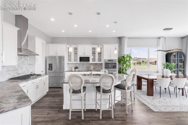 19887 Kershaw Ct, Monument, CO 80132 - kitchen with stainless steel appliances, wall chimney exhaust hood, a sink, white cabinetry, and a center island with sink