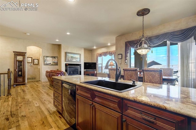 8396 Snow Cap Vw, Colorado Springs, CO 80920 - kitchen featuring dishwashing machine, a sink, light wood finished floors, open floor plan, and arched walkways