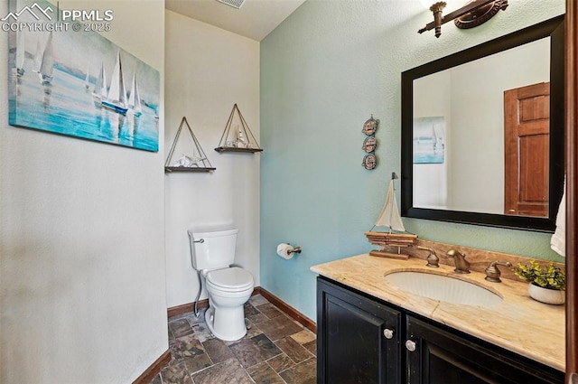 half bathroom featuring stone tile floors, baseboards, toilet, and vanity