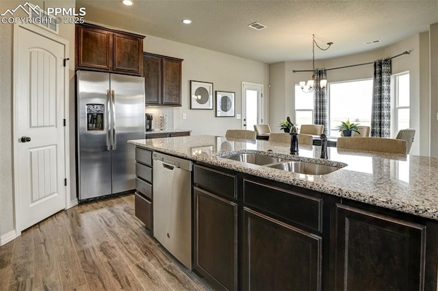 kitchen with appliances with stainless steel finishes, a sink, a chandelier, light wood-type flooring, and dark brown cabinets