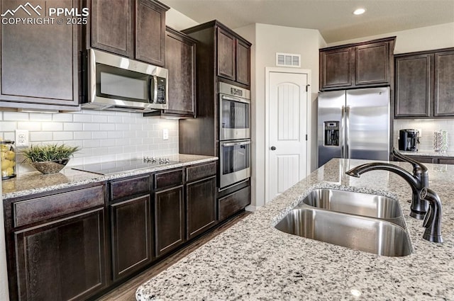 kitchen featuring stainless steel appliances, a sink, dark brown cabinetry, light stone counters, and recessed lighting