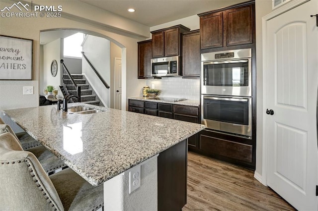 kitchen with stainless steel appliances, a kitchen bar, light stone countertops, a sink, and wood finished floors