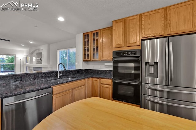 kitchen with appliances with stainless steel finishes, a sink, glass insert cabinets, recessed lighting, and dark stone countertops