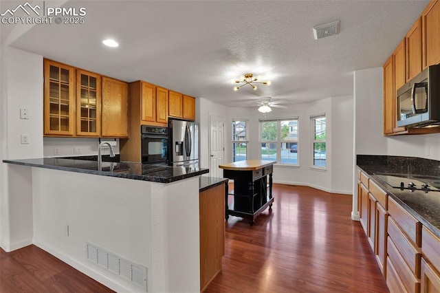 kitchen with black appliances, dark wood finished floors, a peninsula, baseboards, and brown cabinets
