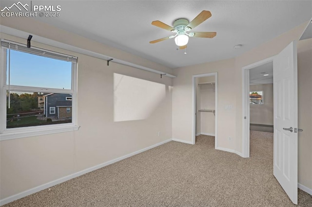 unfurnished bedroom featuring carpet flooring, baseboards, a walk in closet, a closet, and a ceiling fan