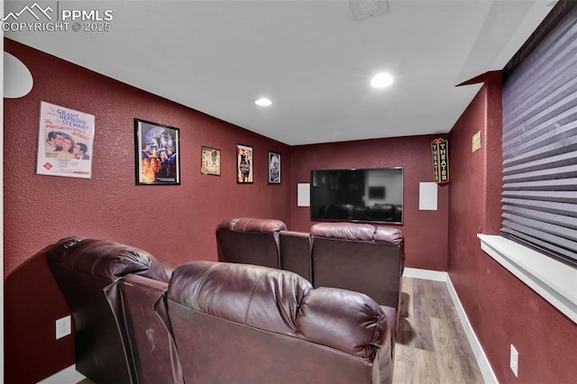 home theater featuring light wood finished floors, recessed lighting, a textured wall, and baseboards